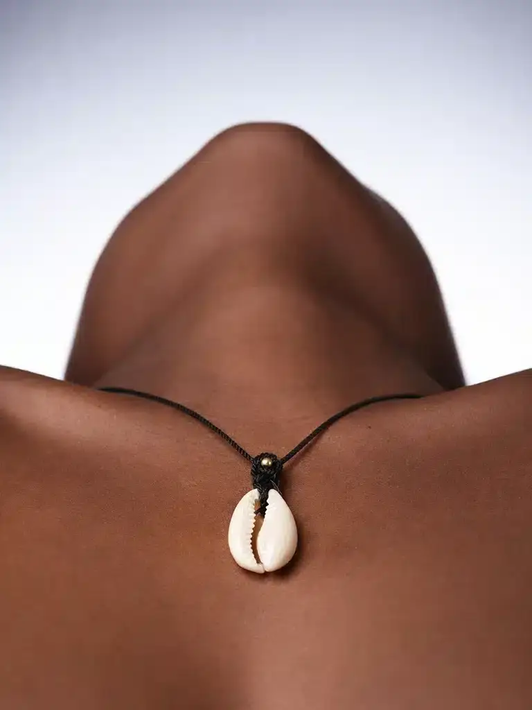 Livraison offert dès 60€ d'achat Une femme noir porte sensuellement un collier en coquillage de cauri et micro macramé