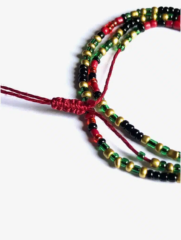 Bracelet artisanal multi-rangs composé de petites perles rouges, vertes, noires et dorées, monté sur un cordon ajustable rouge, présenté sur un fond blanc.