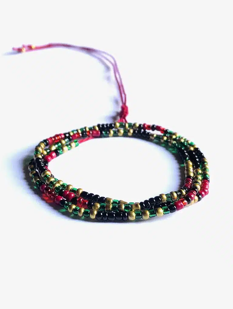 Bracelet artisanal multi-rangs composé de petites perles rouges, vertes, noires et dorées, monté sur un cordon ajustable rouge, présenté sur un fond blanc.